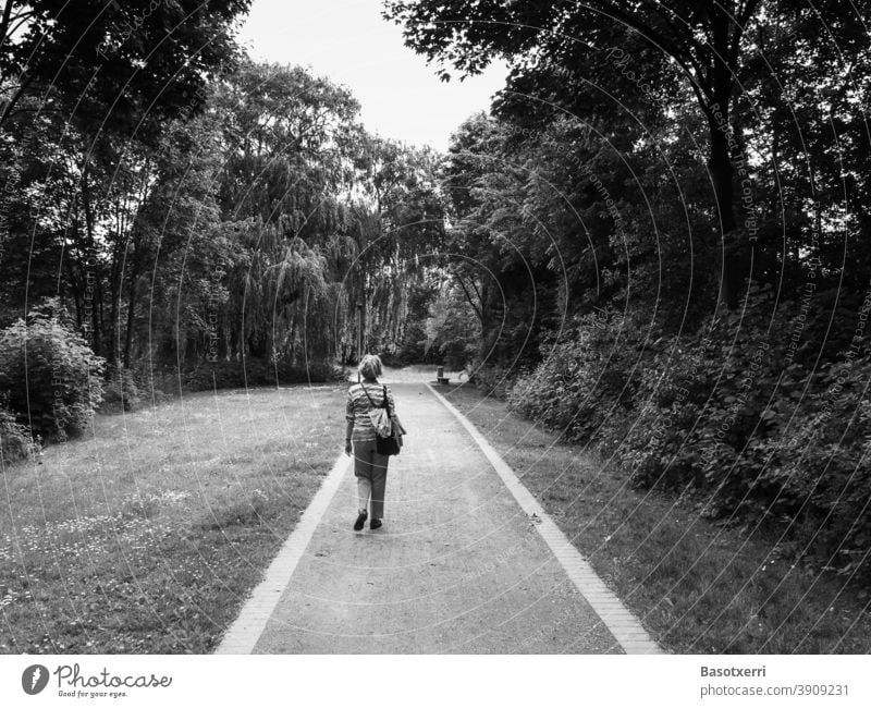 Ältere, aber moderne Dame auf einem Weg durch einen Stadtpark (Schwarz-Weiß-Aufnahme) Belm Osnabrück Niedersachsen Deutschland Park Schotter Schotterweg