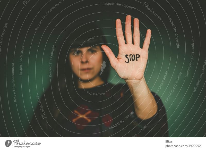 Frau streckt ihre ausgestreckte Hand, auf dem das Wort Stop steht, in die Kamera. Nein sagen, Grenzen aufzeigen. Ablehnung Gestik böse sich wehren nein