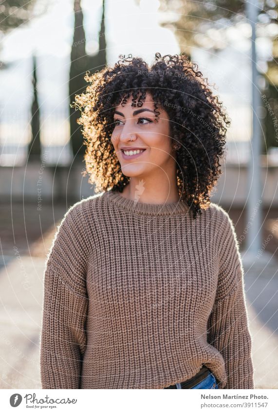 Schöne Frau mit lockigem Haar in einem Park, die einen beigen Pullover trägt und lächelt. Sonnenlicht Mode Porträt Afro-Look echte Frau Mensch Ethnizität Frisur