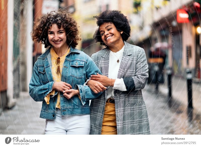 Freunde spazieren im Regen Tag in die Kamera schauen laufen Straße Frauen multiethnisch Afro-Mädchen Kaukasier Porträt Spaß haben Vorderansicht Freundschaft