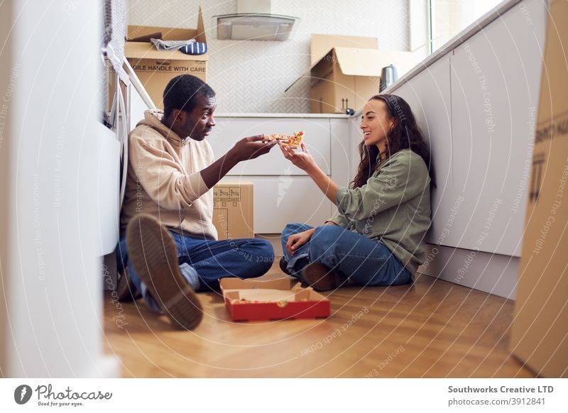 Junges Paar feiert den Umzug in ein neues Haus, das auf dem Boden sitzt und Pizza in der Küche mit Umzugskartons isst junges Paar Hauskauf Imbissbude zu feiern