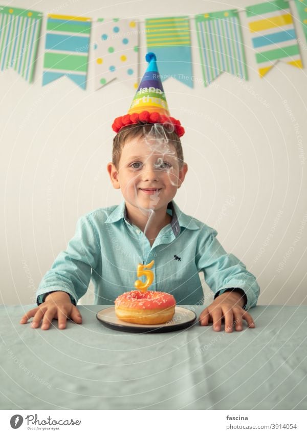 Kind durch Rauch von Kerze auf festlichen Donut Geburtstag Krapfen Junge Hände fünf Jahr sein wenig Lächeln Halt Teller Doughnut in die Kamera schauen Spaß