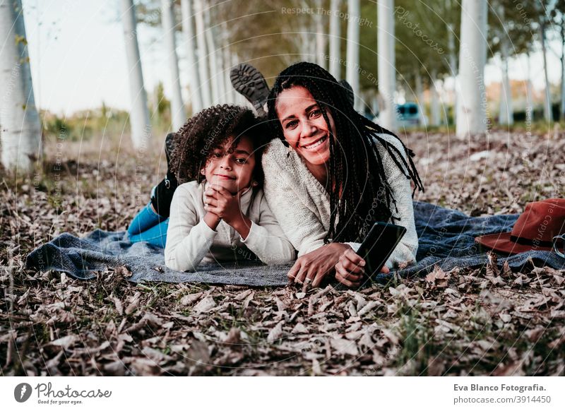 hispanische Mutter und afro Kind Mädchen im Freien liegen auf Decke. Herbst-Saison. Familie und Liebe Konzept Umarmung Afro-Look Frau Tochter Sonnenuntergang