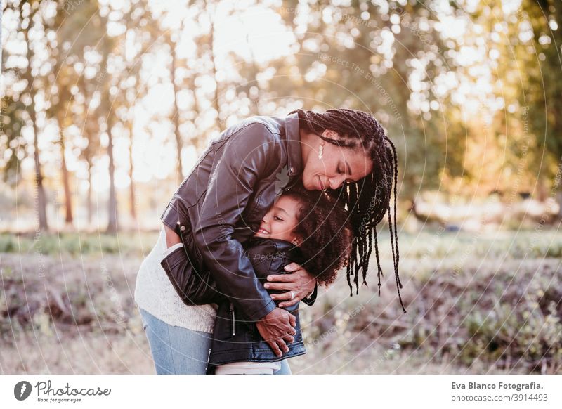 hispanische Mutter und afro Kind Mädchen im Freien umarmen bei Sonnenuntergang während der goldenen Stunde. Herbstzeit. Familie und Liebe Konzept Umarmung