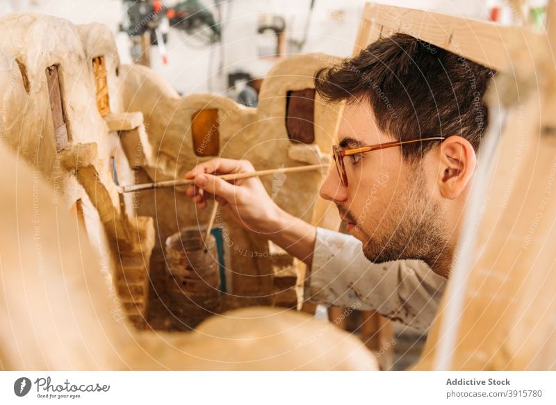 Handwerker, der ein Miniaturmodell eines Lehmhauses im Atelier herstellt Ton Werkstatt Mann Haus Model Gebäude Kunstgewerbler Farbe kreieren männlich Hobby