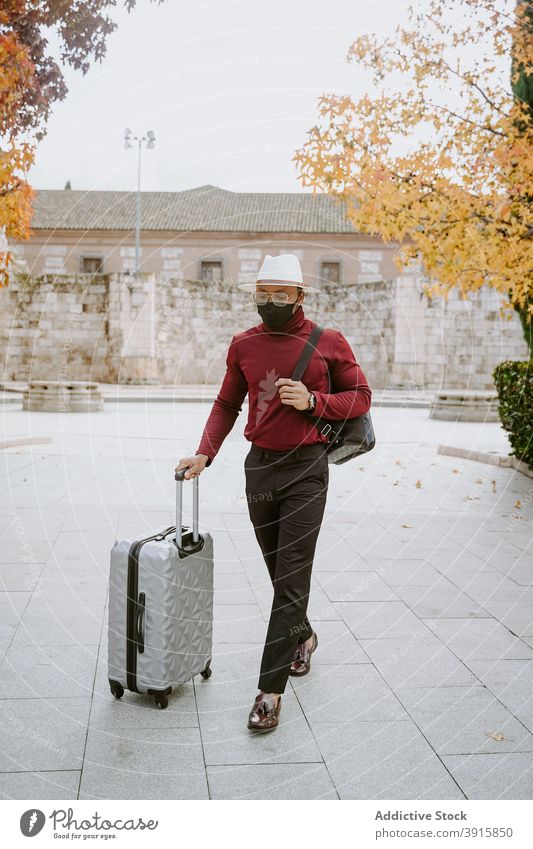 Reisender schwarzer Mann in Maske zu Fuß in der Stadt mit Koffer Großstadt Gepäck elegant Spaziergang ankommen Tourist männlich ethnisch Afroamerikaner