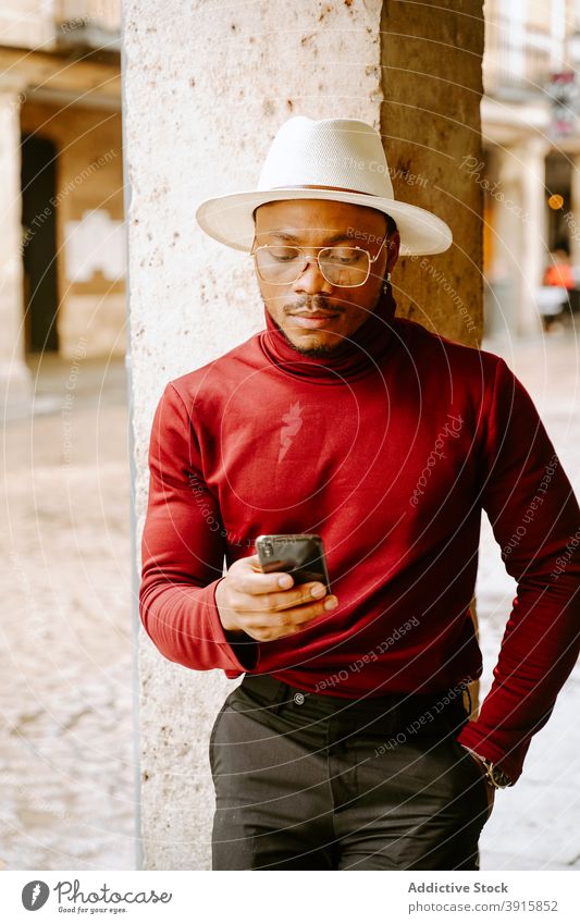 Schwarzer Mann in stilvollem Outfit mit Mobiltelefon in der Stadt elegant Smartphone Stil Großstadt Straße Bestimmen Sie trendy Hut männlich ethnisch Browsen