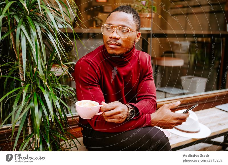 Schwarzer Mann surft auf Smartphone und trinkt Kaffee in der Nähe eines Cafés in der Stadt Browsen Großstadt Surfen soziale Netzwerke Straße Stil trendy