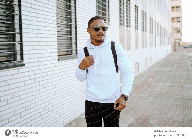 Stilvolle schwarze Mann zu Fuß entlang der Straße an einem sonnigen Tag lässig Spaziergang Großstadt Bestimmen Sie trendy Outfit männlich ethnisch