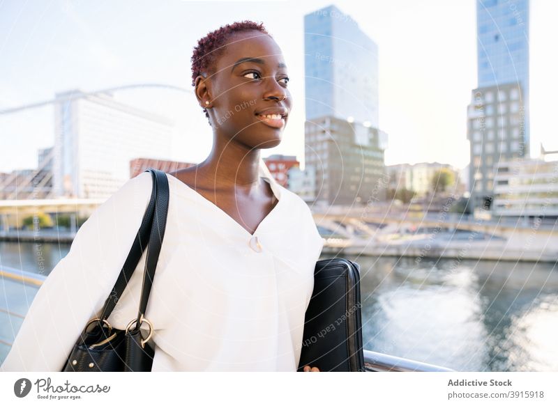 Lächelnde afroamerikanische Geschäftsfrau, die auf einer Stadtböschung steht selbstbewusst positiv modern urban Stil Erfolg Glück jung Großstadt schwarz