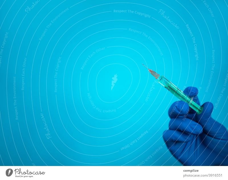 Injektions Spritze und blauer Handschuh vor blauem Hintergrund impfstudie impfzentrum Kanüle steril Tisch Injektionsmittel injektionsspritze Impfpflicht Nadel