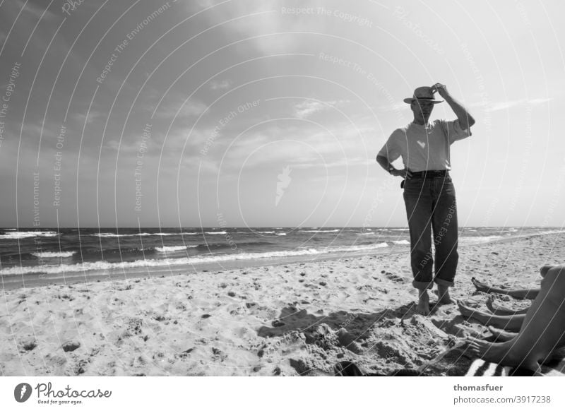 Mann mit Hut am Strand und Füße von einigen Damen bekleidet Hose T-Shirt Meer Wellen Bein Wind Sonne Wolken Schatten Sommerfrische Weite Urlaub Kontakt