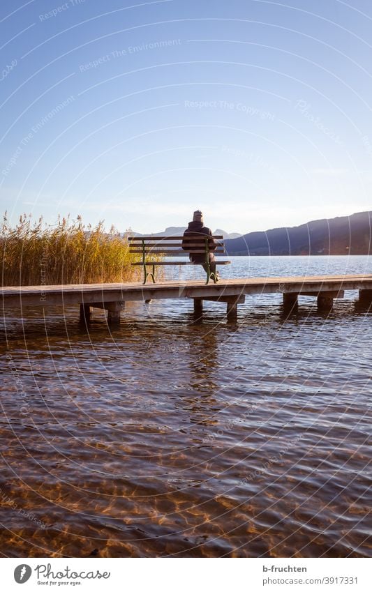 Eine Person sitzt am Steg auf einer Parkbank See Wasser warten ruhig Einsamkeit Erholung Seeufer Himmel Natur Landschaft Herbst Österreich Idylle Schönes Wetter