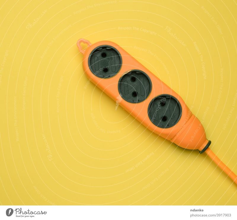 Gummi orange Powerstrip mit drei Steckdosen isoliert auf einem gelben Hintergrund Streifen Vorrat Werkzeug Draht Adapter Kabel Nahaufnahme Anschluss Schnur