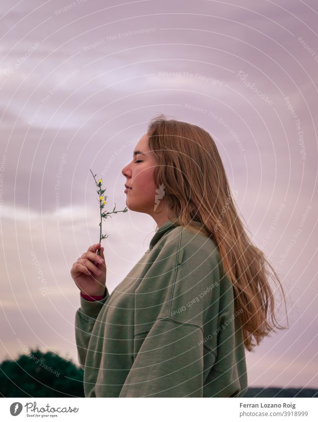 Porträt einer Frau, die an einer Blume riecht Behaarung braune Haare lange Haare geschlossene Augen riechen riechend rosa Himmel hoddie Blumen Natur Park