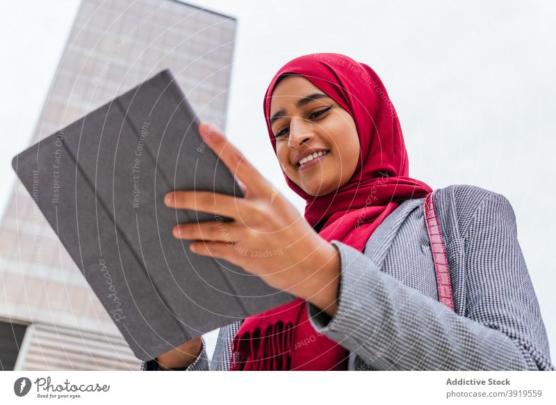 Positive ethnische Frau mit Kopftuch verwendet Tablette auf der Straße Browsen Hijab muslimisch Großstadt Lächeln Surfen benutzend arabisch jung rot Farbe Gerät