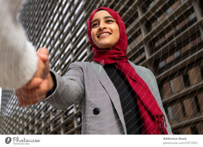 Lächelnde ethnische Geschäftsfrau im Hijab schüttelt die Hand des Partners Hände schütteln Business Großstadt heiter Unternehmer Kopftuch Tradition Frau