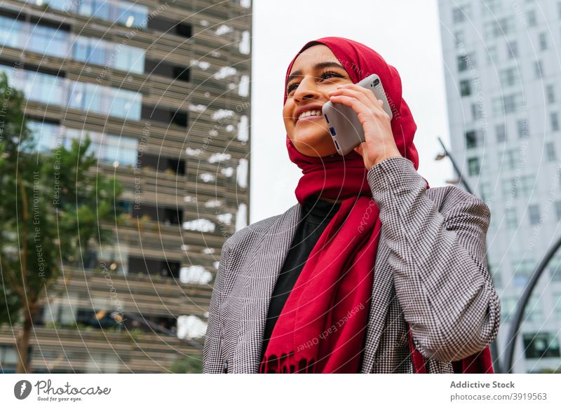 Erfreute ethnische Frau in Hijab spricht auf Smartphone in der Stadt Kopftuch reden heiter sprechen Großstadt Tradition Straße arabisch Mobile Telefon benutzend