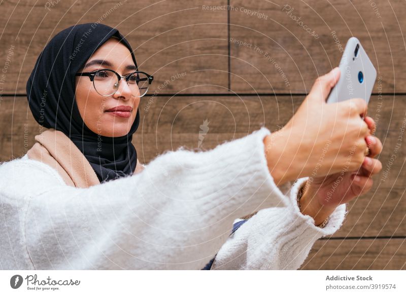 Charmante ethnische Frau in Hijab unter Selfie in der Stadt Kopftuch Smartphone fotografieren Gedächtnis Großstadt Lächeln charmant arabisch Straße Foto Telefon