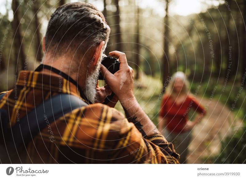 Älterer Mann, der mit der Kamera eine Frau im Wald fotografiert fotografierend Fotokamera Senior reif Zusammensein wandern Lifestyle Freizeit im Freien