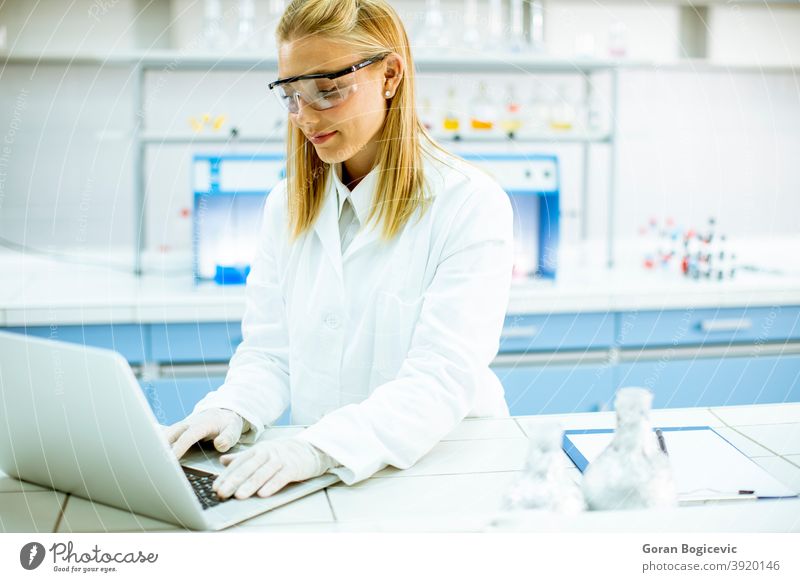 Weibliche Forscherin in weißem Laborkittel und Schutzbrille mit Laptop bei der Arbeit im Labor Analysieren Hintergrund Biografie Chemikalie Chemiker Klinik