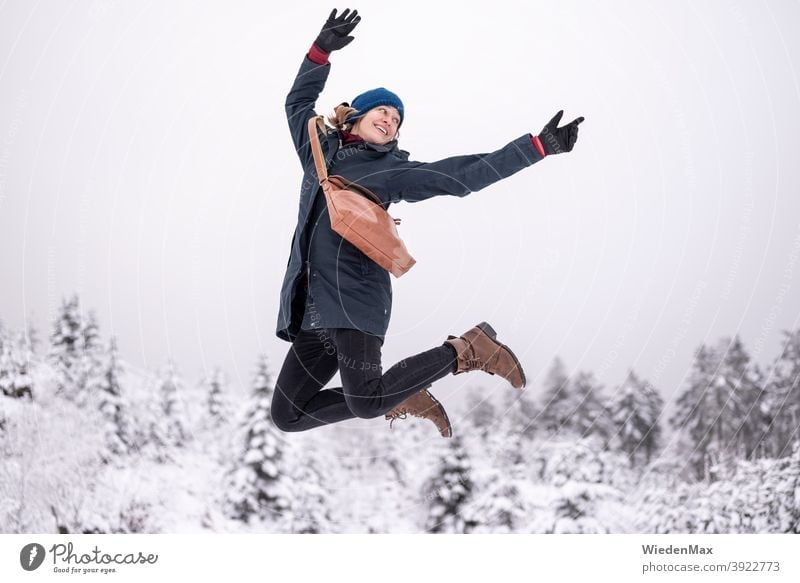 Eine junge Frau freut sich über den ersten Schnee und macht einen Luftsprung Winter Freude Glück glücklich Balletttänzer kalt