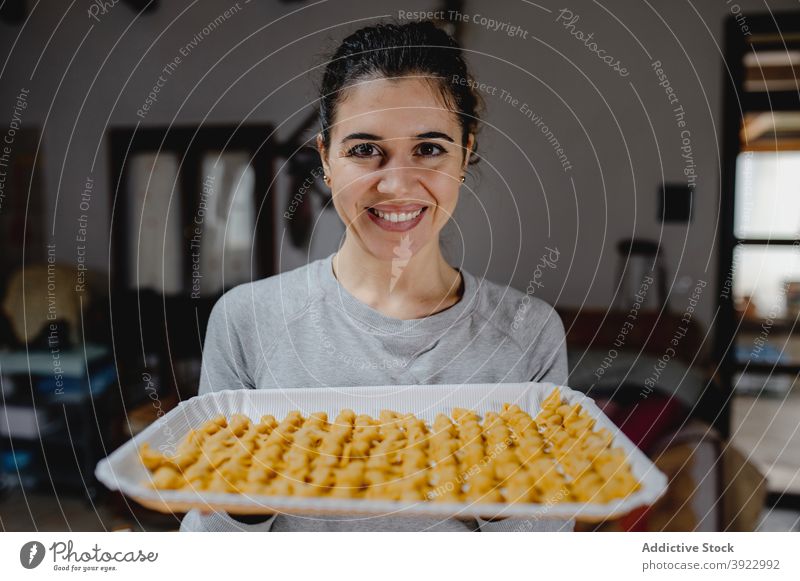 Zufriedene Frau mit Tortellini auf Backblech Koch selbstgemacht Tradition Italienische Küche Knödel Teigwaren roh Lächeln vorbereiten Bestandteil heiter Tisch