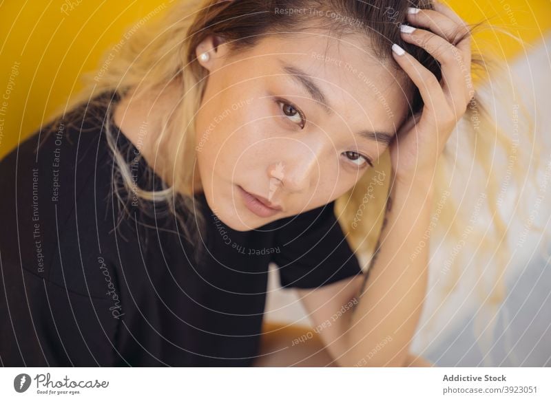 Junge ethnische Frau sitzt in der Nähe von gelben Wand Hipster jung urban Straße Stil Farbe Teenager modern asiatisch gefärbtes Haar tausendjährig Lifestyle