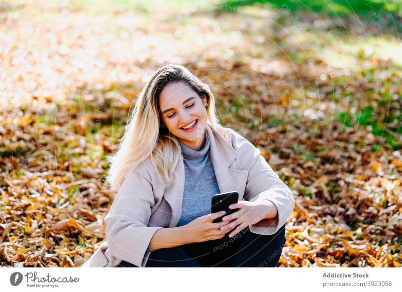 Positive Frau sendet Nachricht auf Handy im Park sprechen Smartphone genießen Gespräch heiter Herbst Apparatur Inhalt Gerät Funktelefon Glück Optimist Dame froh