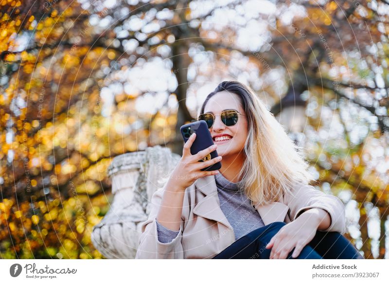 Positive Frau sendet Nachricht auf Handy im Park sprechen Smartphone genießen Gespräch heiter Herbst Apparatur Inhalt Gerät Funktelefon Glück Optimist Dame froh
