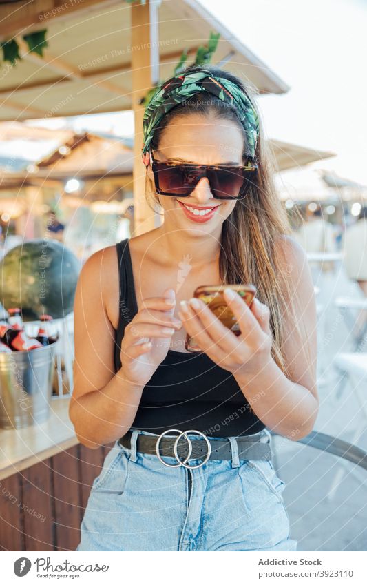 Glückliche Frau, die in einer Bar im Freien auf ihrem Mobiltelefon surft Smartphone benutzend Sommer tropisch heiter Browsen Telefon Sonnenbrille Nachricht