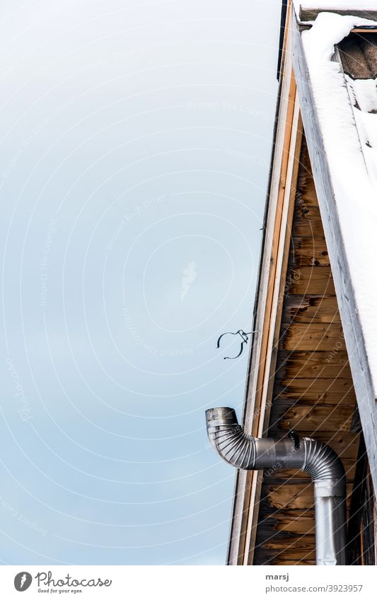 Die Rohrschelle am Dachgiebel einer einfachen Hütte wartet auf die Vollendung des Ofenrohrs oder zumindest eine sinnvolle Nutzung Heizungsrohr Eis Winter kalt