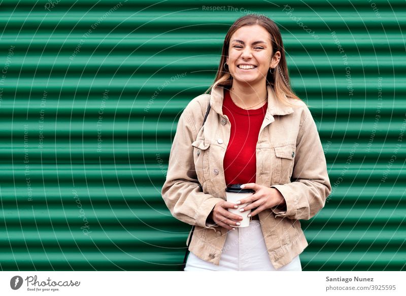 Glückliches junges Mädchen Porträt in die Kamera schauen Tasse Kaffee grüner Hintergrund Stehen hübsch Frau außerhalb im Freien Vorderansicht posierend