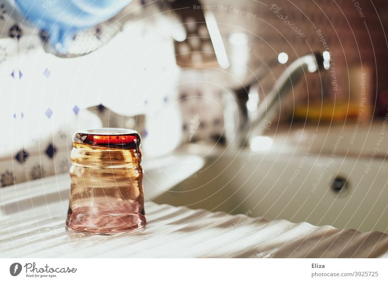 Ein Wasserglas wird nach dem Abwasch neben dem Waschbecken zum Trocknen abgestellt. Glas Geschirrspülen ordentlich trocknen Gaukler Sonne Küche Haushalt gespült