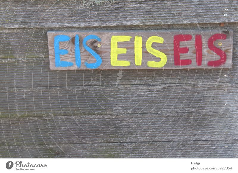 EIS EIS EIS - Das Wort EIS handgeschrieben in blau, gelb und rot auf einem Brett an einer Holzwand Eis Buchstaben Schrift Handschrift Werbung Schriftzeichen