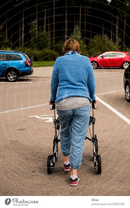 Eine Frau mit Gehbehinderung schiebt ihren Rollator über einen Behindertenparkplatz Behinderung Handicap Mensch Mobilität schieben