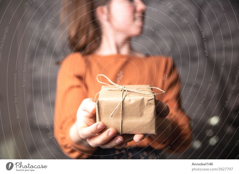 Junge Frau hält eine kleine Handwerkspapier-Geschenk-Box, schlichtes braunes Papier für Recycling und Geschenk. Geburtstag, Valentinstag Konzept präsentieren