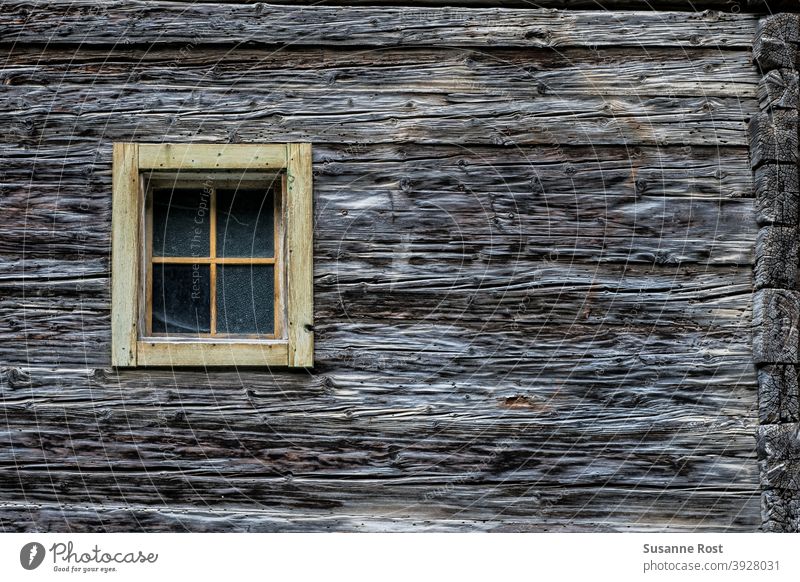 Detailansicht einer Holzfassade aus dicken Holzbalken und mit einem kleinen Sprossenfenster Fenster Fassade Holzfenster alt Wand Detailaufnahme Hütte ländlich