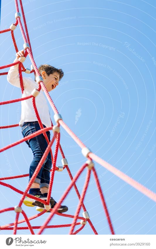Lustiger Junge beim Klettern auf einem Spielplatz aktiv Aktivität Abenteuer Gleichgewicht Blauer Himmel Mut Kaukasier Kind Kindheit Kinder Klettergerüst Farbe
