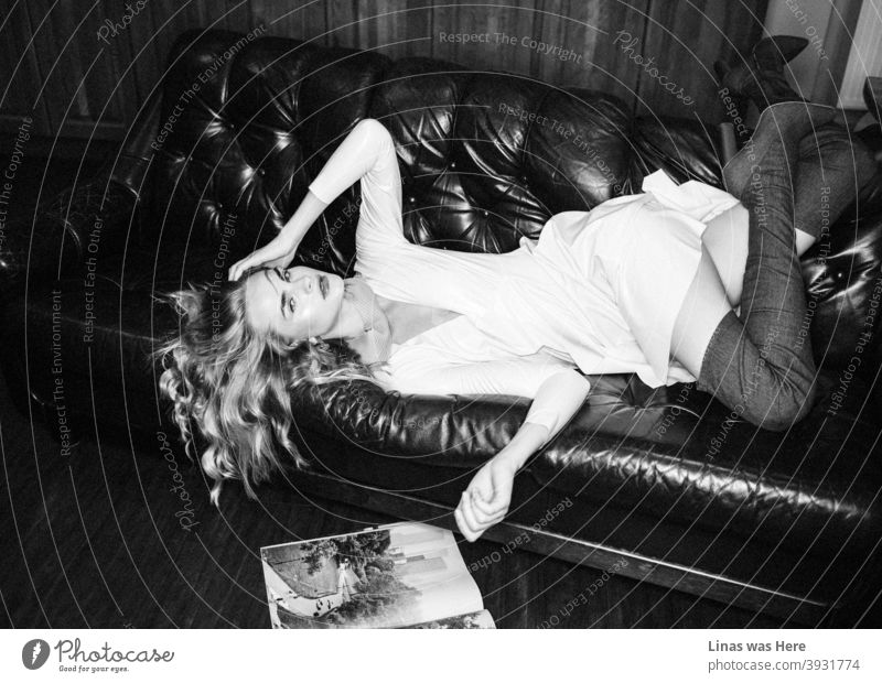 Ein Modeshooting mit einem hinreißenden weiblichen Model in einem weißen Latexkleid. Mit ihren High-Heels fällt sie die Couch hinunter. Einige Zeitschriften liegen auf dem Boden. Dieses schöne Mädchen weiß, wie man posiert.