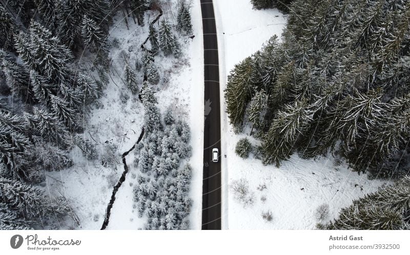 Luftaufnahme mit einer Drohne von einer Straße mit einem Auto das im Winter durch den Wald fährt luftaufnahme drohnenfoto auto winter straße fahren schnee wald