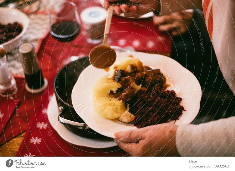 Oma serviert leckeres Essen am gedeckten Tisch - Hirschgulasch, Knödel und Blaukraut. deftig Weihnachtsessen Gulasch Rotkohl Klöße Fleisch Mittagessen Feiertag