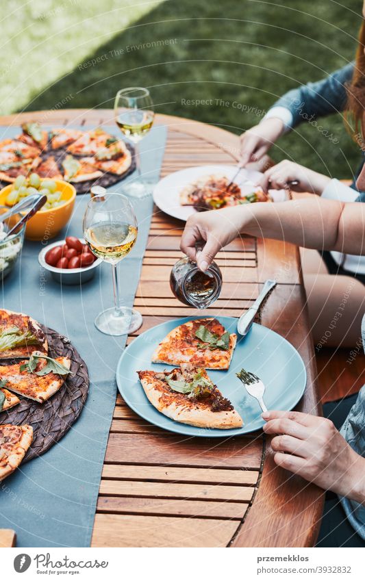 Familie und Freunde mit Mahlzeit - Pizza, Salate, Früchte und trinken Weißwein während Sommer-Picknick im Freien Abendessen in einem Haus Garten Hinterhof