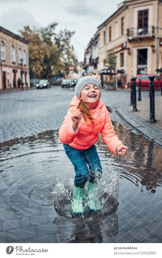 Kleines Mädchen mit großem Regenschirm in der Hand springt an einem verregneten, düsteren Herbsttag in die Pfütze im Freien wenig saisonbedingt fallen Kindheit