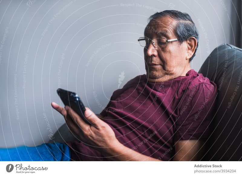 Älterer Mann beim Surfen auf dem Smartphone zu Hause Browsen Senior benutzend Nachricht heimwärts sich[Akk] entspannen Sofa älter männlich ethnisch Liege Raum