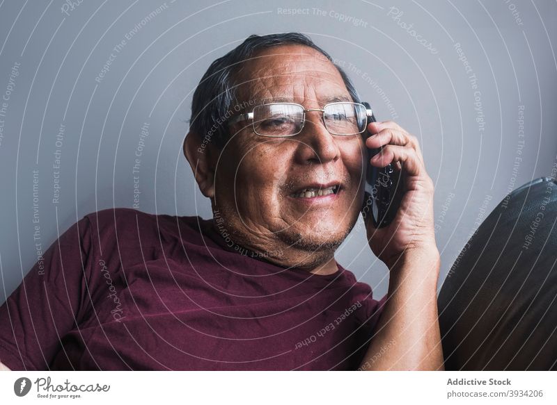 Ethnischer älterer Mann, der zu Hause mit seinem Smartphone spricht sprechen Senior reden heimwärts Mobile Telefon Sofa männlich ethnisch Anruf Liege Rentnerin