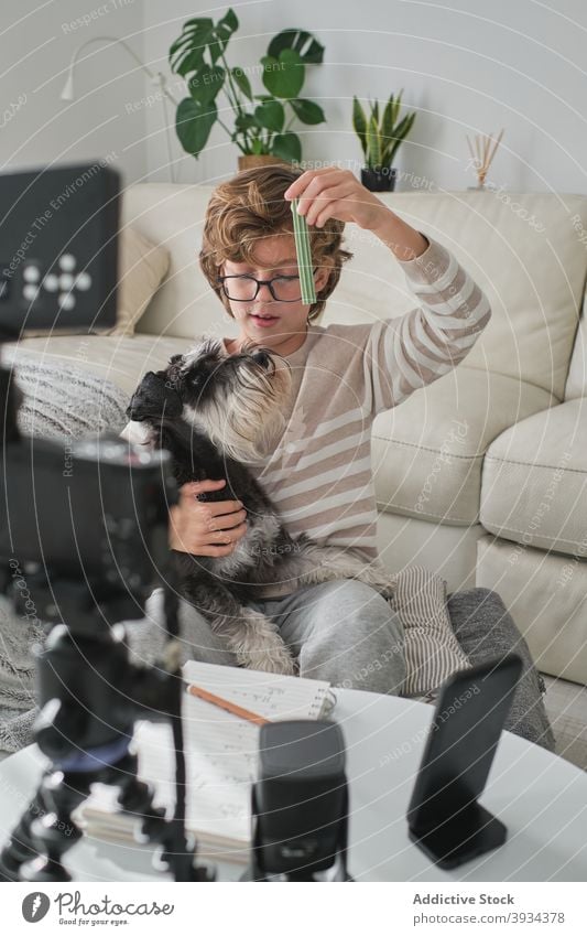 Junger Junge filmt Video mit seinem Hund Spielen spielerisch füttern Aufnahme Wohnzimmer Dreharbeit youtuber Glück Lächeln heiter Spaß haben zu Hause Kind