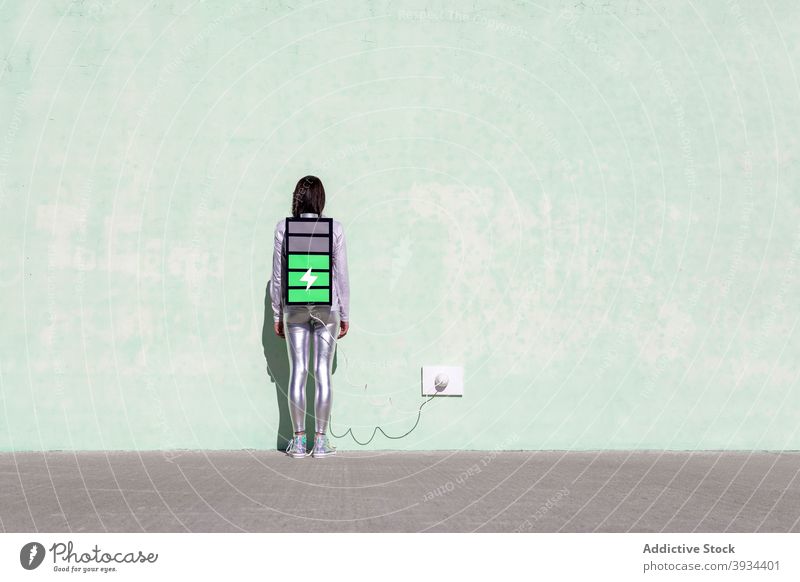 Anonyme Frau mit kreativem großen Batterierucksack, der den Ladevorgang anzeigt Rucksack Gebühr laden Energie digital Konzept Anschluss Straße Wand Schatten