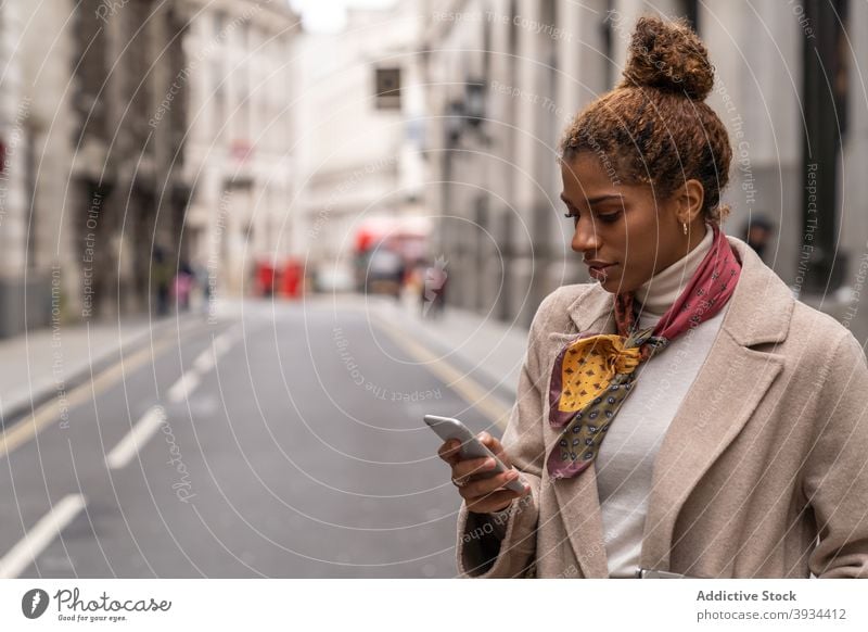 Stilvolle junge ethnische Frau Messaging auf Smartphone beim Gehen auf der Straße Spaziergang benutzend Unternehmer Arbeit Nachricht Laptop Großstadt Browsen