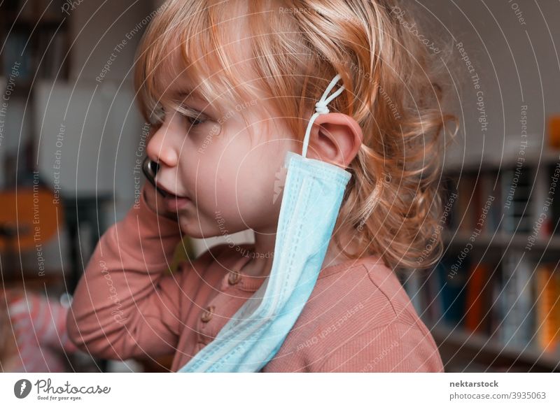 Kind mit Gesichtsmaske aus dem Ohr hängend Mundschutz Frau Mädchen im Innenbereich heimwärts zu Hause Kaukasier schützend 2020 Sperrung Quarantäne reales Leben